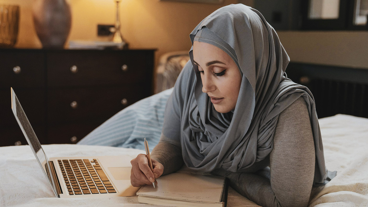 A student reading materials from a laptop and writing notes