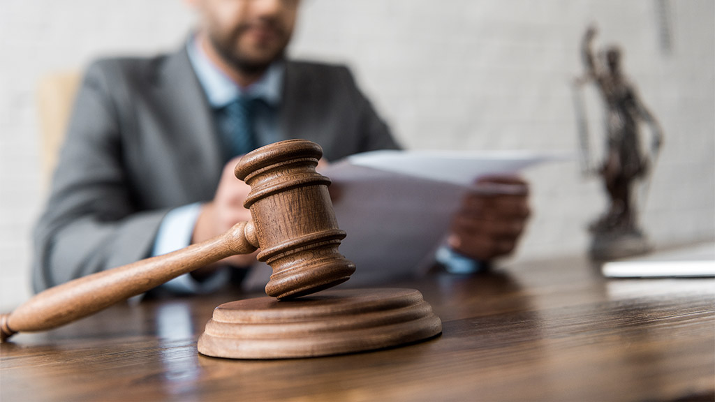 close-up view of wooden hammer and judge working with papers behind