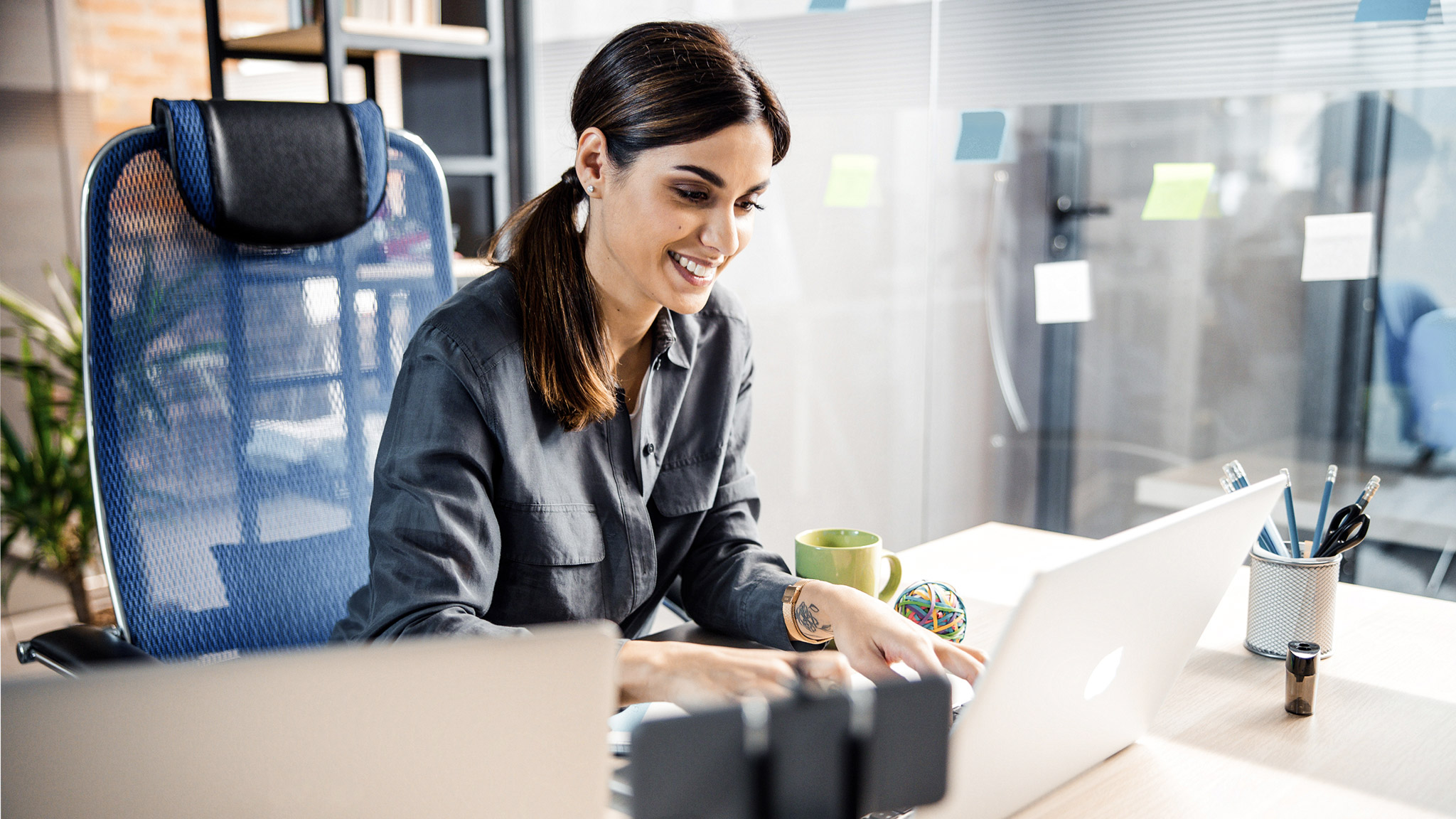 brunette female keeping smile on her face while typing message on her laptop