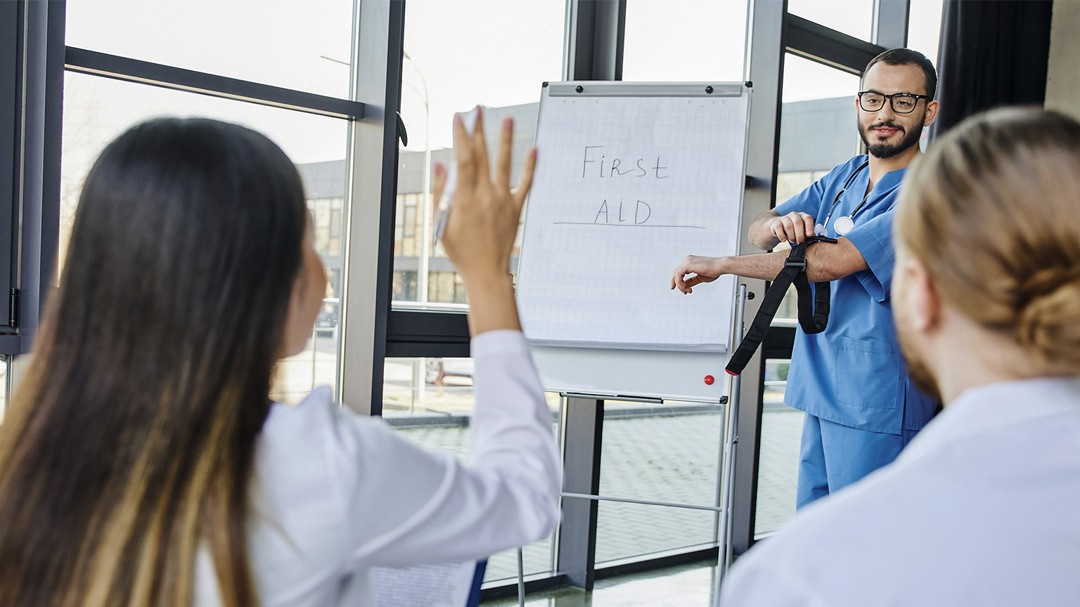 medical instructor with compressive tourniquet standing at flip chart and looking at student asking question during first aid seminar, emergency preparedness