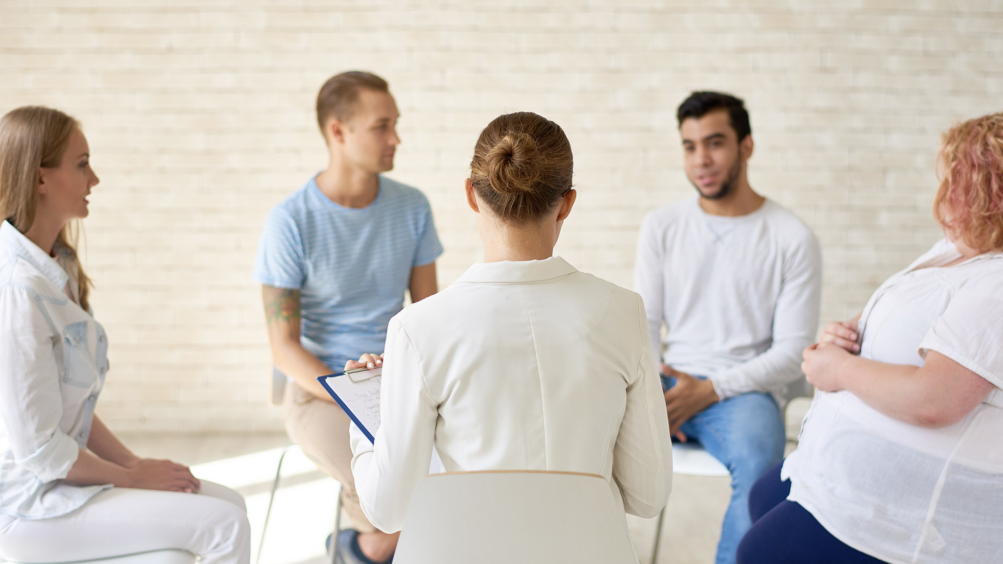  female coach working with group of young people sitting in circle during therapy session