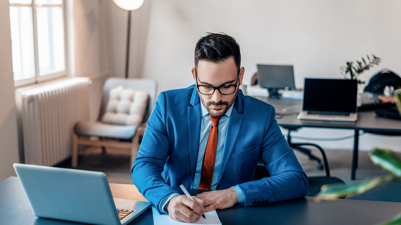 Young handsome businessman writing notes on paper in modern office.