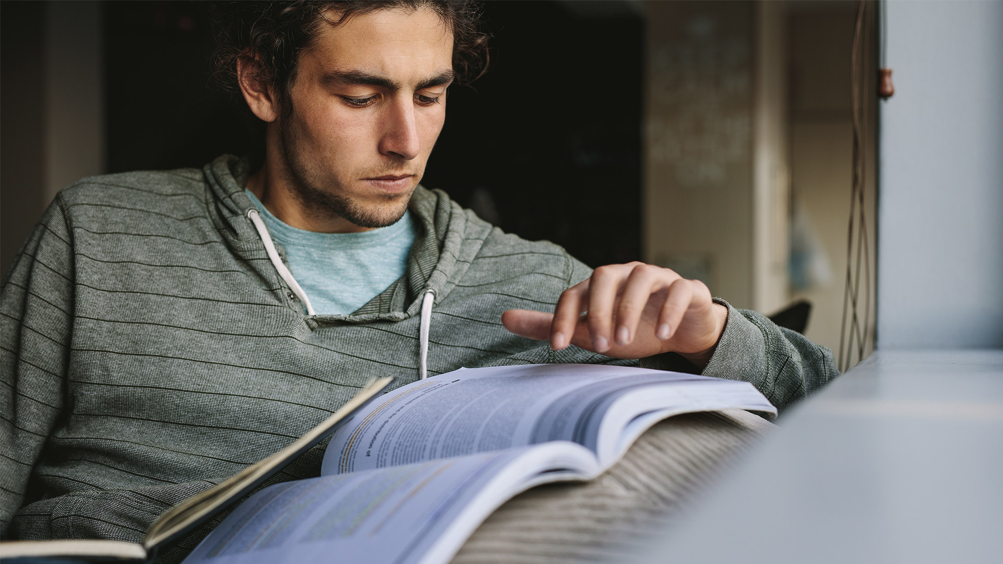 Student reading a book and writing notes sitting on a couch.