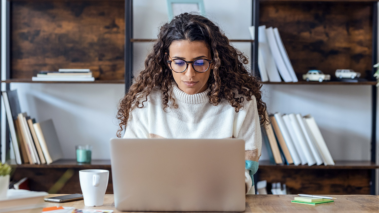 Shot of concentrated beautiful business woman working with laptop while drinking coffee in living room at home.