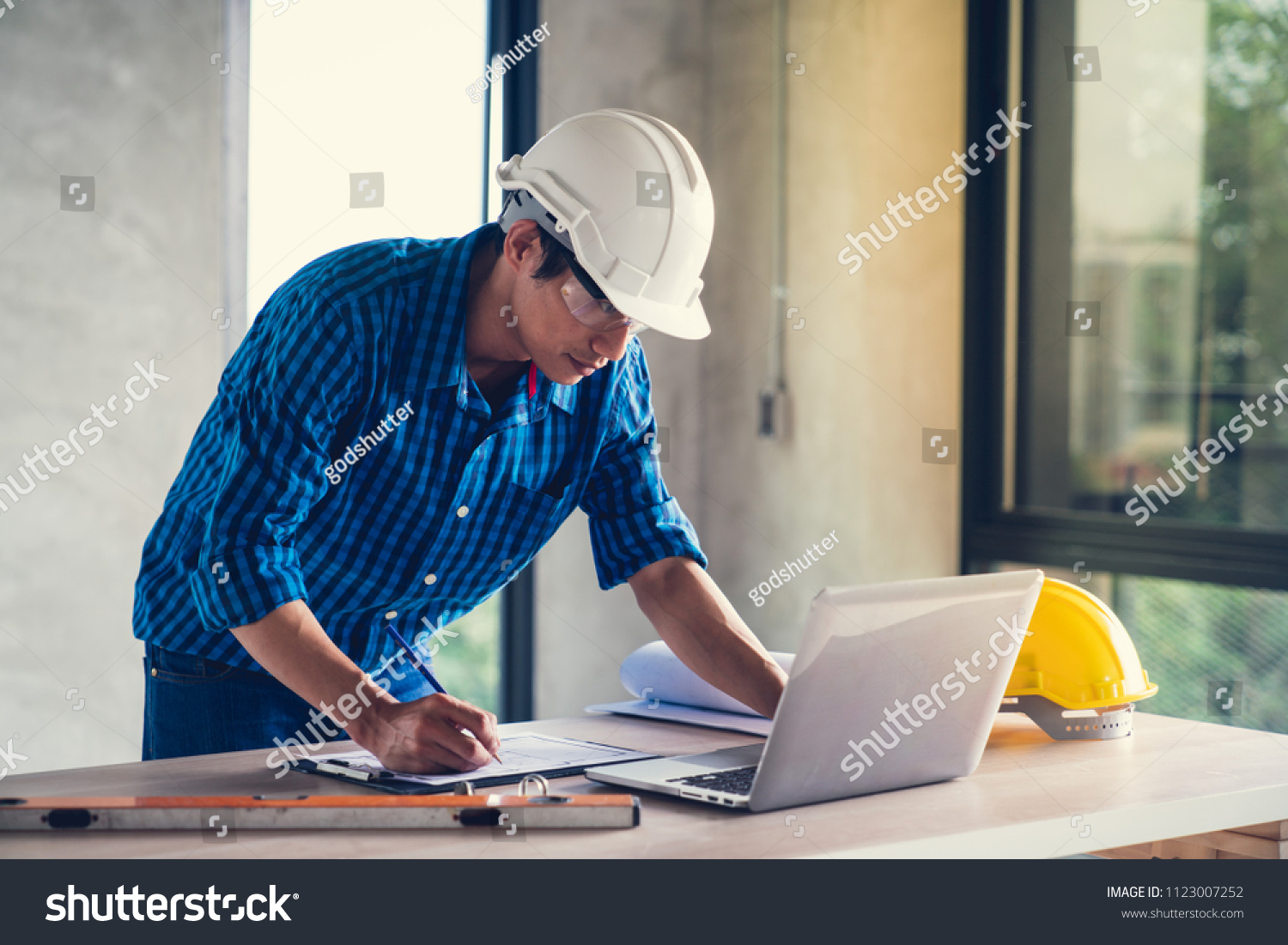 A young man wearing a hard hat preparing Working Documents on a table. 