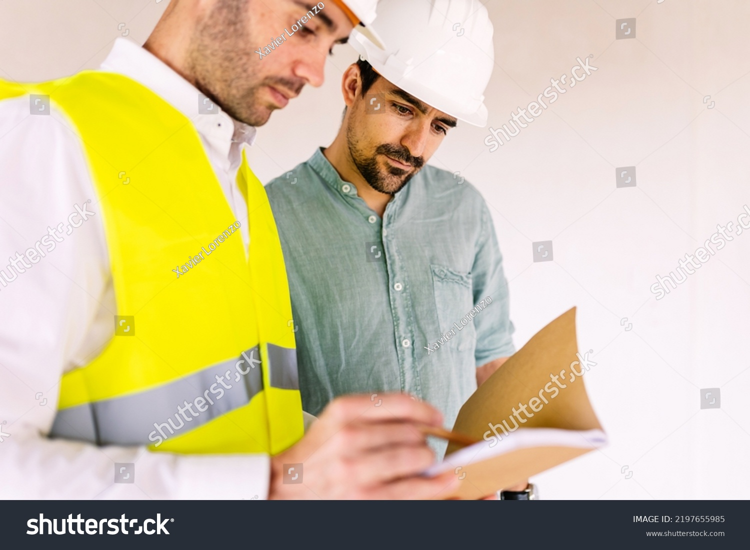 Two construction workers collaborating on something out of a book.