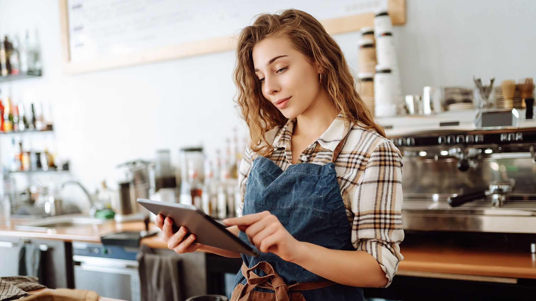 A young woman in an apron with a digital tablet at the bar counter of a coffee shop