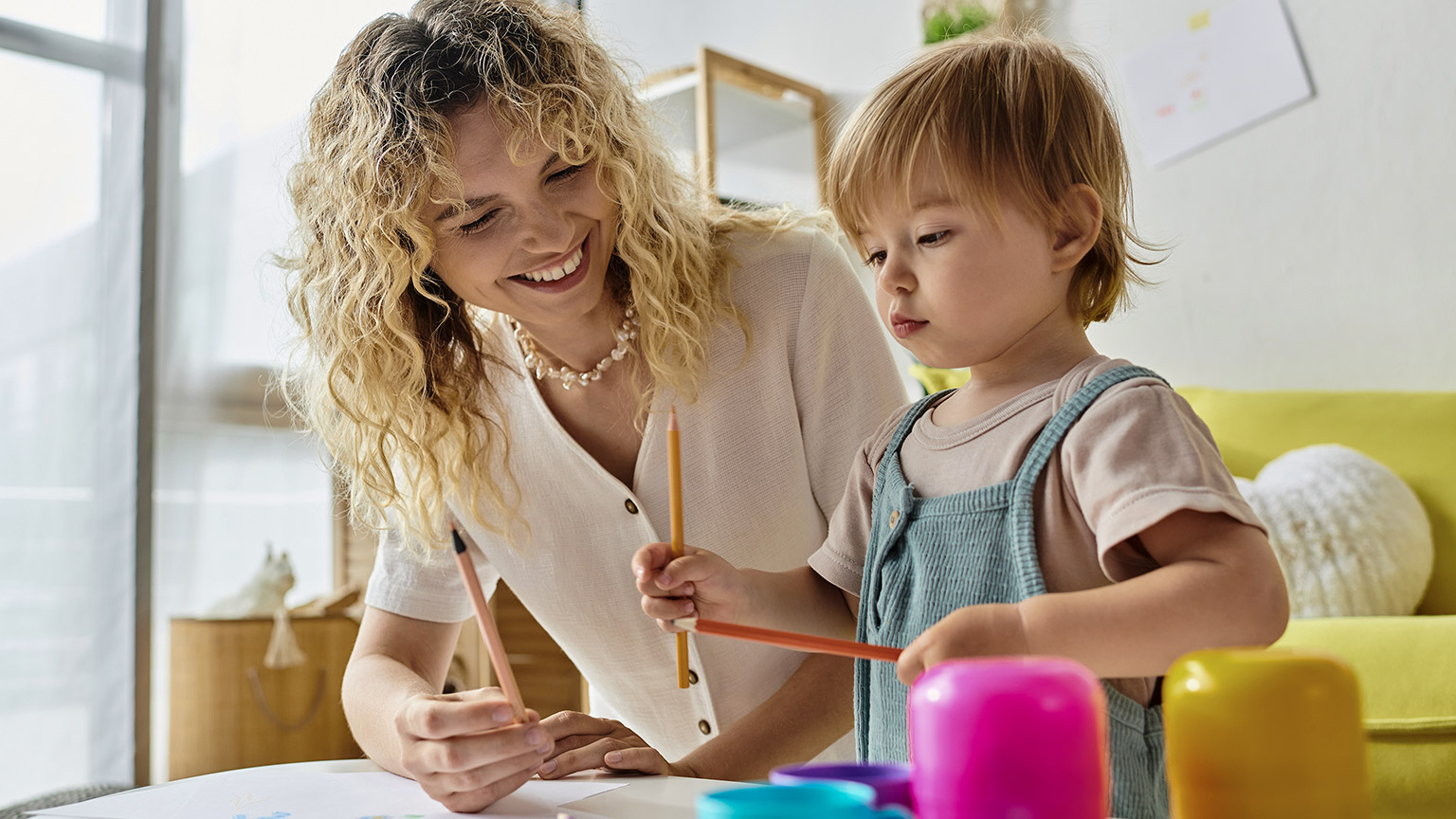 A curly-haired mother and her toddler daughter explore creativity using colored pencils in a cozy home setting