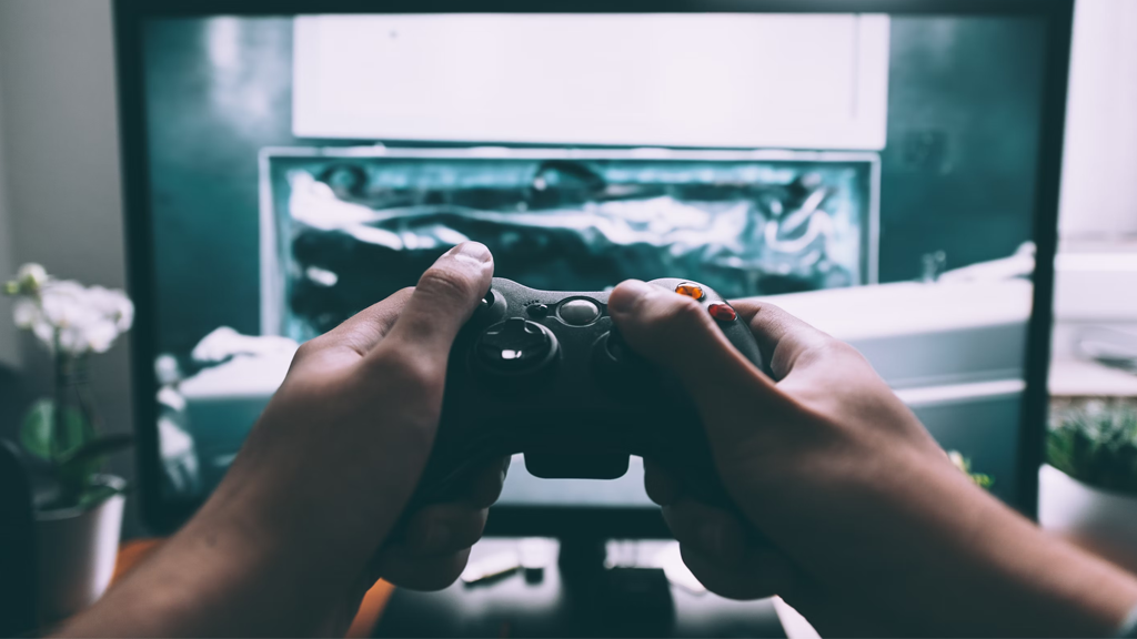 pair of hands holding a xbox 360 controller in front of a computer monitor