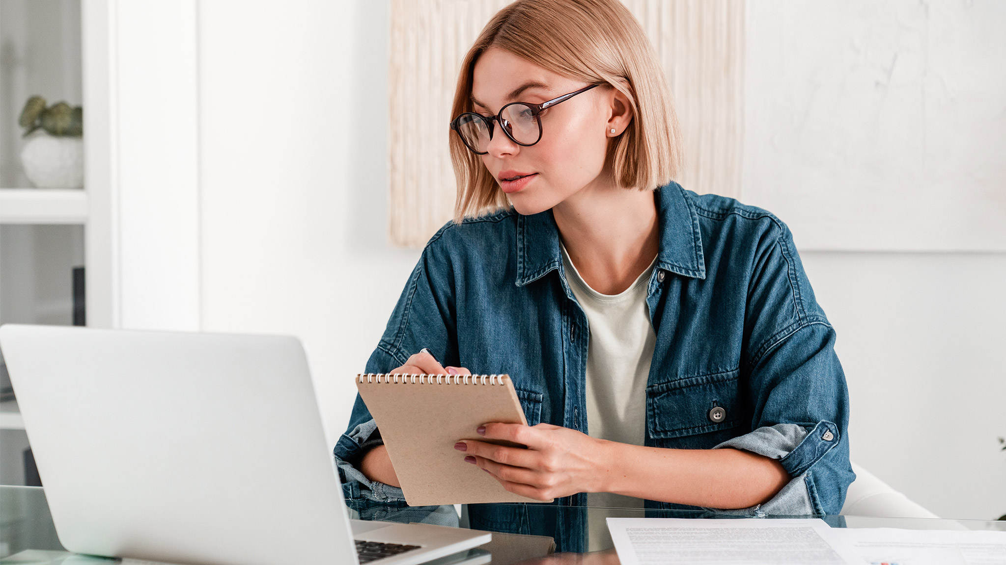 Young woman taking notes using laptop for remote studies at home desk