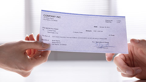 Close-up Of Woman's Hand Holding Cheque And Giving To Man