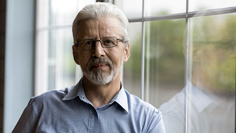 Head shot portrait mature grey haired man wearing glasses standing near window