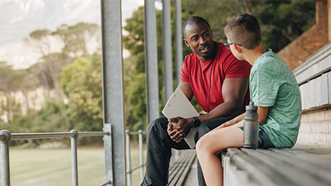 School coach talking a young student while sitting outside.