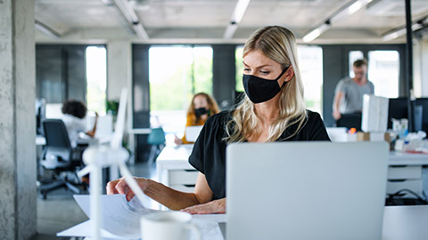 Young woman with face mask back at work in office after lockdown, working.