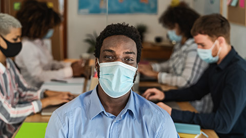 African man wearing face mask in co-working creative space with team work