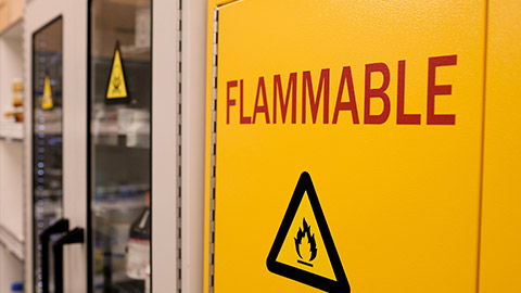 Close up black flammable sign with red letter flammable on doors of yellow flammable cabinet in laboratory room