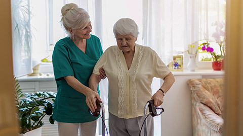 Nursing assistant helping senior woman with walking frame