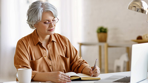 woman with laptop and notebook while sitting at table and working