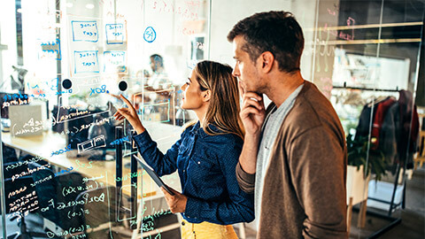 Two colleagues drawing up a flow chart with a calk pen, on a glass wall