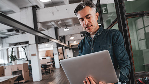 A senior designer standing in a modern office with his laptop