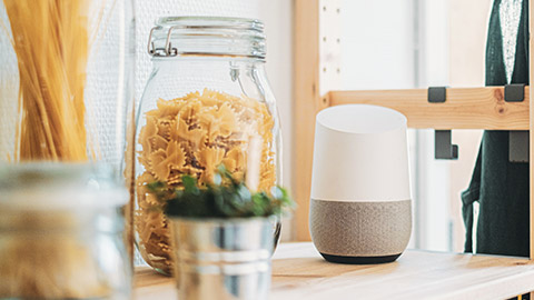 A Google Alexa smart speaker sitting on a shelf next to a jar of pasta