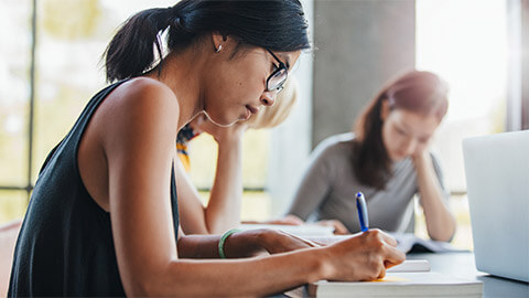 A young student seated at a desk, taking down notes