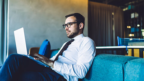 A professional seated on a comfortable sofa, absorbing economic data on their laptop