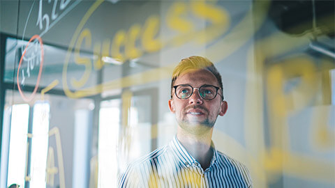 A person brainstorming the concept of entrepreneurial behaviour with chalk markers on a glass wall