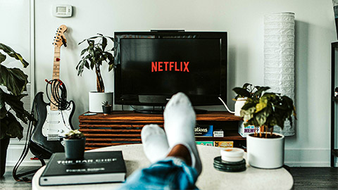 A person seated on their sofa with their feet on the coffee table, about to watch something on Netflix