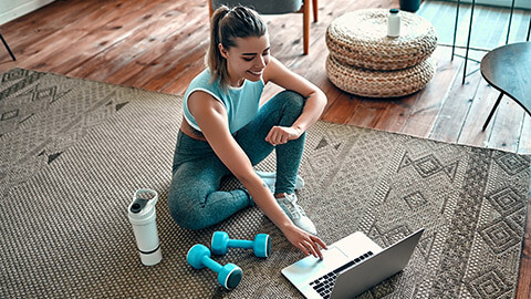 An active person sitting on the floor about to workout with a protein shake and weights beside them.