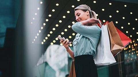 A shopper standing outside a shopping complex while checking for other deals on her mobile phone