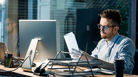 Casual man in eyeglasses looking through papers working in office