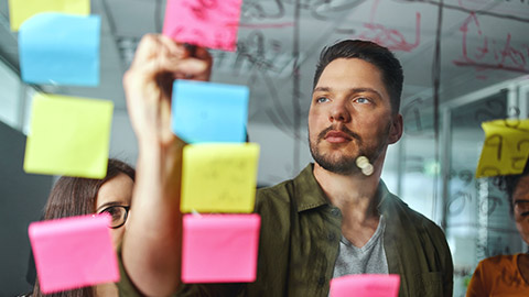 A person writing on a sticky note on a glass wall