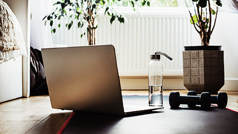 A laptop with a dumbell and bottle of water on a yoga mat