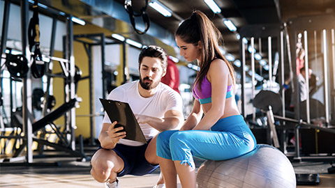 Woman sitting on the gym ball while talking with trainer