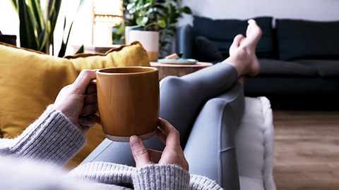 POV of young woman relaxing at home with cup of coffee lying on couch