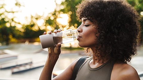 frican american sportswoman drinking water while working out on sports ground