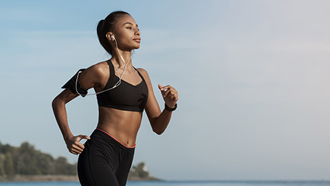 Side view shot of young woman in sportswear jogging on beach