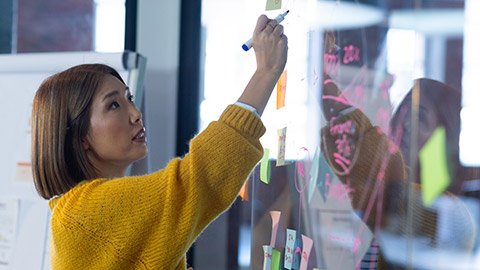 businesswoman standing in front of glass wall and writing in office