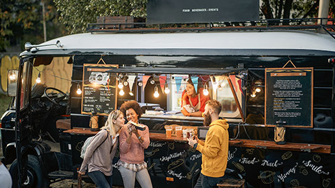 multiethnic group of young people socializing while eating outdoor in front of modified truck for fast food