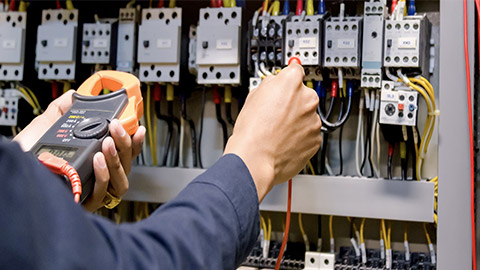 Electrician engineer work tester measuring voltage and current of power electric line in electical cabinet control.