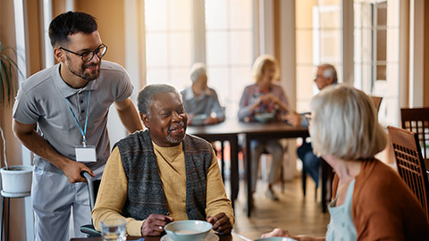 Happy senior people and their caregiver talking in dining room at nursing home.