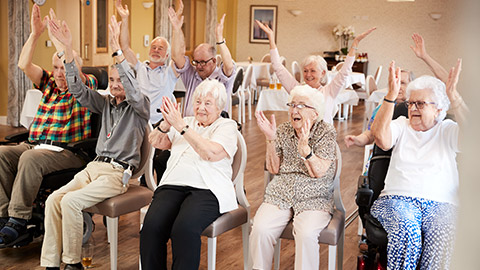 Carer Leading Group Of Seniors In Fitness Class In Retirement Home