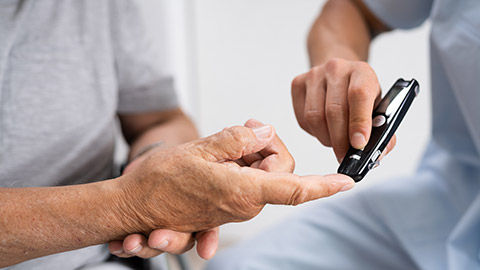 A carer doing a blood sugar test for an elderly patient