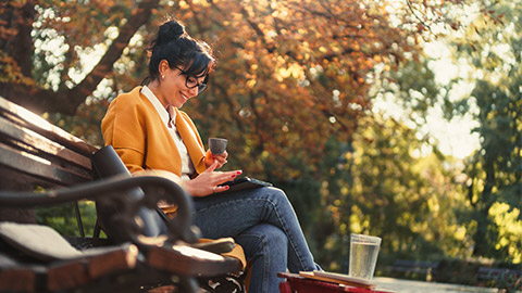 Young beautiful business woman working on a tablet sitting on the bench in the park