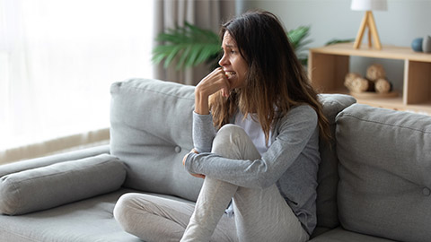 Frustrated unhappy woman crying, sitting on couch at home alone