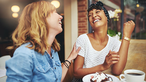 2 friends enjoying a laugh over cake and coffee