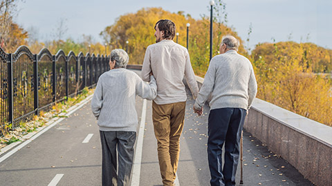 An elderly couple walks in the park with a male assistant or adult grandson