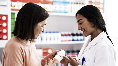 Two women pharmacist and customer holding pills bottle at pharmacy