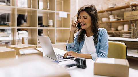 entrepreneur speaking on the phone while working on a laptop in her warehouse